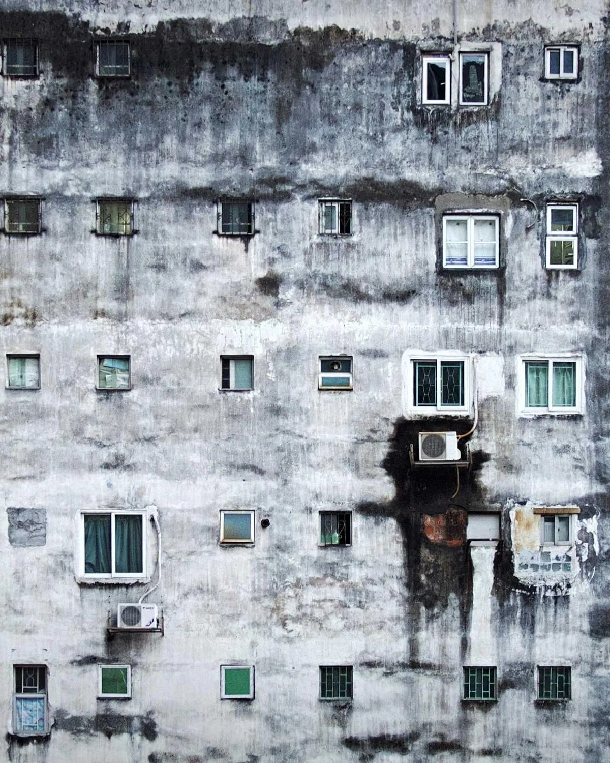A concrete building facade with a single lit window at dusk.